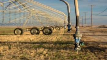 Photo of a crop sprayer or irrigator in a dried filed. There is a close up on one of the sprayer nozzles. 