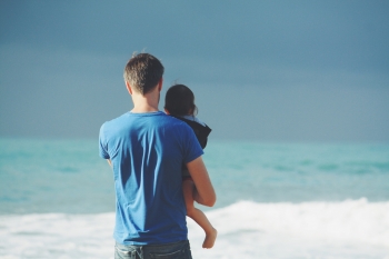 A father holds his child in front of the ocean.