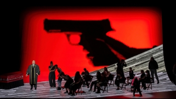 Scene from The Walkers with a group of people gathered in front of a red backdrop with a gun.