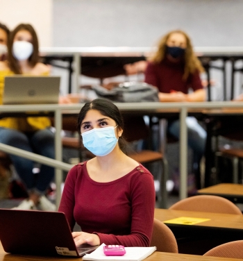 Woman in front of a computer in a mask in a classroom