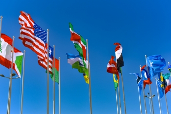 Flags of various countries flying in the wind against the backdrop of a bright blue sky.