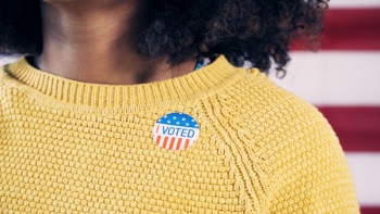 An African-American woman wears a "I Voted" sticker on a yellow sweater