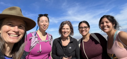 Nancy Grimm and ESSA (Earth Systems Science for the Anthropocene) scholars smile against a blue sky background while on a hike. 