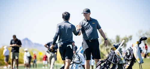 A golf coach smiles and clasps hands with a student-athlete on a golf course