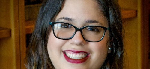 Headshot of Christina Grey in glasses and a black blouse smiling at the camera.