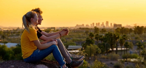 Two people sit on a rock and watch the sunset