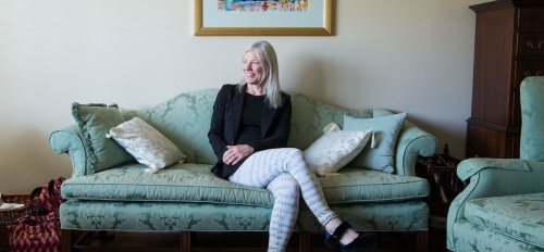 ASU Professor Devoney Looser is pictured seated on a sofa in her living room in her house.