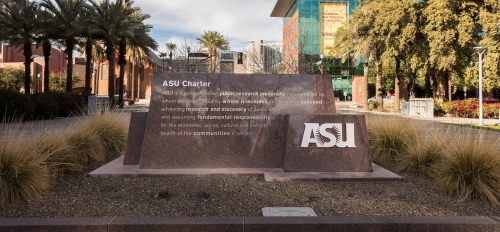 A sign showing the ASU charter with buildings behind it.