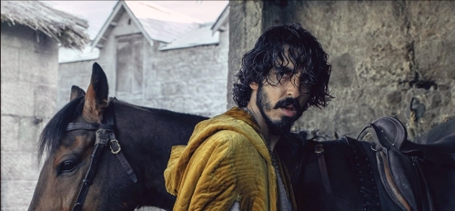 Actor Dev Patel stands in front of a horse and looks over his shoulder in a photo still from the film "The Green Knight"
