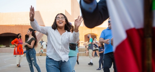 A woman waves her hands and smiles while dancing in a museum courtyard