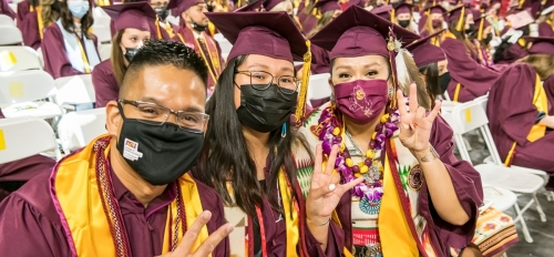 ASU College of Health Solutions graduates wearing caps and gowns at their convocation ceremony while making the pitchfork gesture.