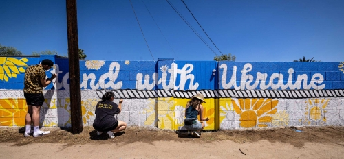 People painting a mural on a wall that says "Stand with Ukraine"