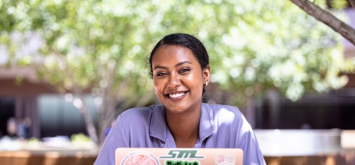 Sabrina Mehari, a student at ASU's Barrett, The Honors College, smiling while seated at a picnic table with a laptop.