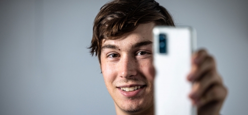 A man smiles while holding a phone up toward the camera
