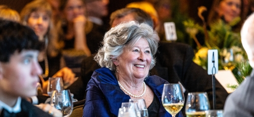 Woman seated at a table in a crowd, smiling.