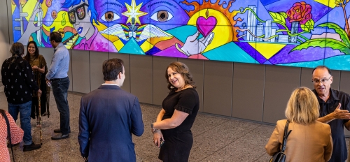 People socializing in lobby with bright, colorful mural displayed on wall behind them