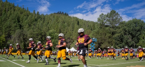 ASU football players on a field surrounded by pine trees