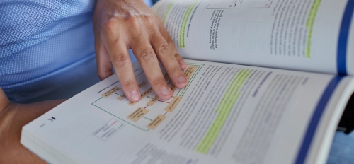 A hand holding a textbook open to a page with highlighted text.