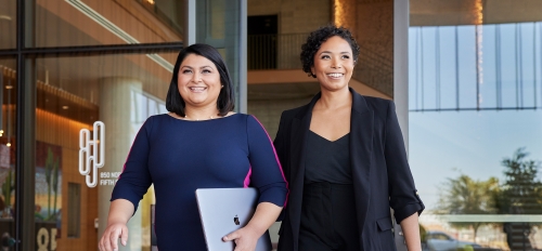 Two women in business attire walk out of a building