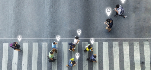 Aerial view of people walking across crosswalk with location icons next to them.