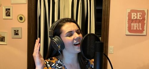 Amanda Stone in a recording studio singing into a microphone with headphones on.