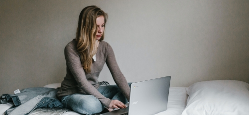 A woman works on a laptop while sitting on a bed