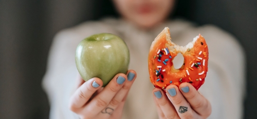 Woman holding out an apple and a donut.