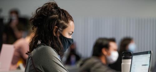 woman wearing a mask in a classroom while using a laptop