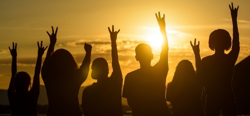 Silhouettes of six people giving the forks up hand signal in front of a sunset