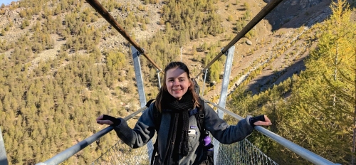 ASU alumna Azalea Thomson smiling on a narrow bridge in Switzerland, with a green, mountainous terrain in the background.