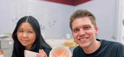 Two ASU Barrett Honors College students hold up painted ceramic bowls and smile.