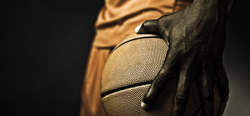 The hand of a Black basketball player gripping a basketball.