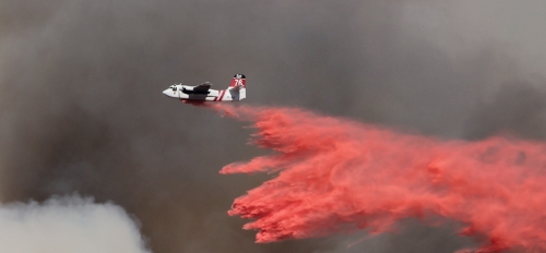 Plane flies through dark clouds dispersing a red substance.