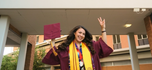 Berenice Pelayo in front of the WP Carey Business School in her cap and gown