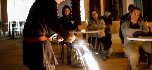 Man demonstrating tools from the Iron Age. Sparks fly from the tool as students look on.