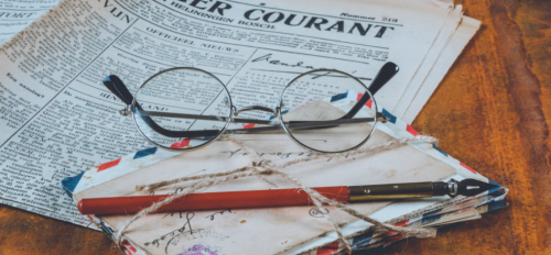 round-framed glasses sitting on a pile of old letters with a newspaper in the background