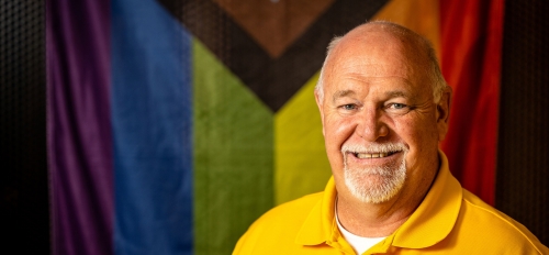 Man's portrait in front of an LGBTQ flag