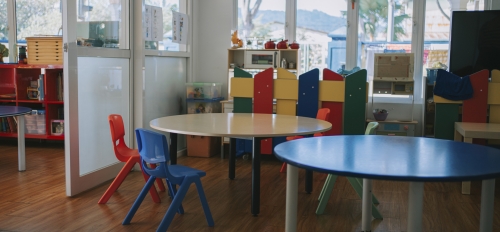 Empty children's tables and chairs in a room with windows.
