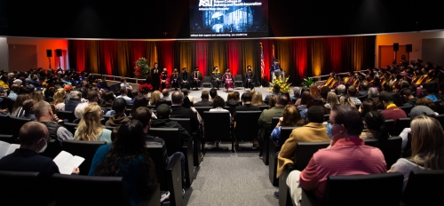 People seated in an auditorium with graduates on the right side in their caps and gowns.