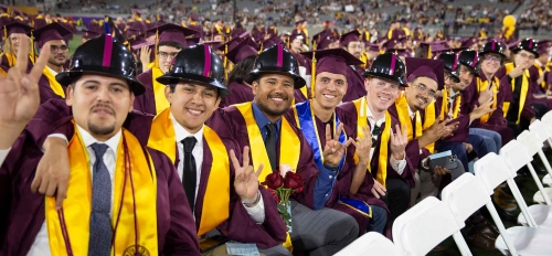 Del E. Webb School of Construction graduates seated in a row wearing graduation attire and hard hats.
