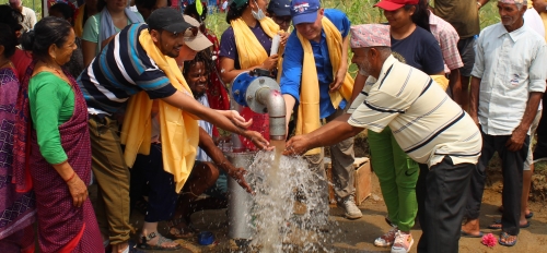 A crowd of people gather around a pipe to put their hands in the water that flows from it.
