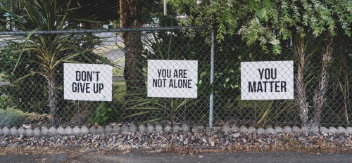 Three poster boards hung on a fence. They read "Don't give up," "You are not alone" and "You matter."