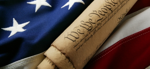 Photo of U.S. Constitution with United States flag in background.