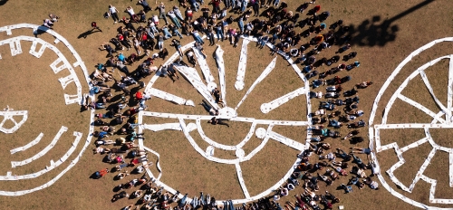Aerial photo of people surrounding a 50-foot-wide flat, circular sculpture made with paper on field.