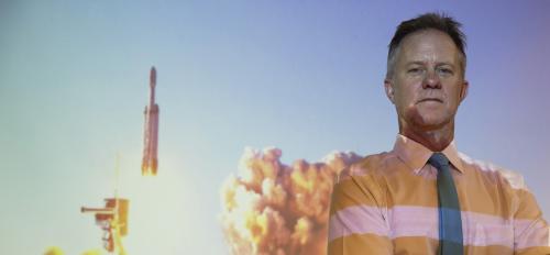 Hugh Barnaby stands in front of a projection of a SpaceX Falcon Heavy rocket launch. 