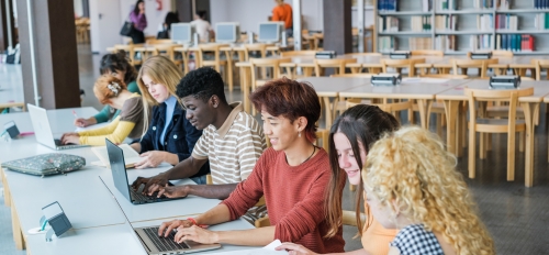 High school students seated at a table working on laptops in a library.