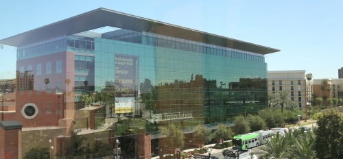 Exterior view of the Fulton Center, a six-story building covered in glass windows, next to University Drive, where cars pass by.