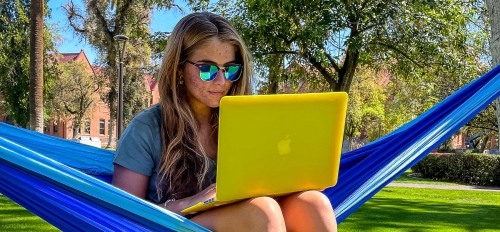 Student sitting in a hammock on ASU's Tempe campus working on a laptop.