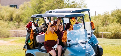 People dressed in marron and gold clothes sitting in a golf cart.