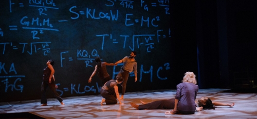 Dancers perform on stage with mathematical equations on a screen behind them.